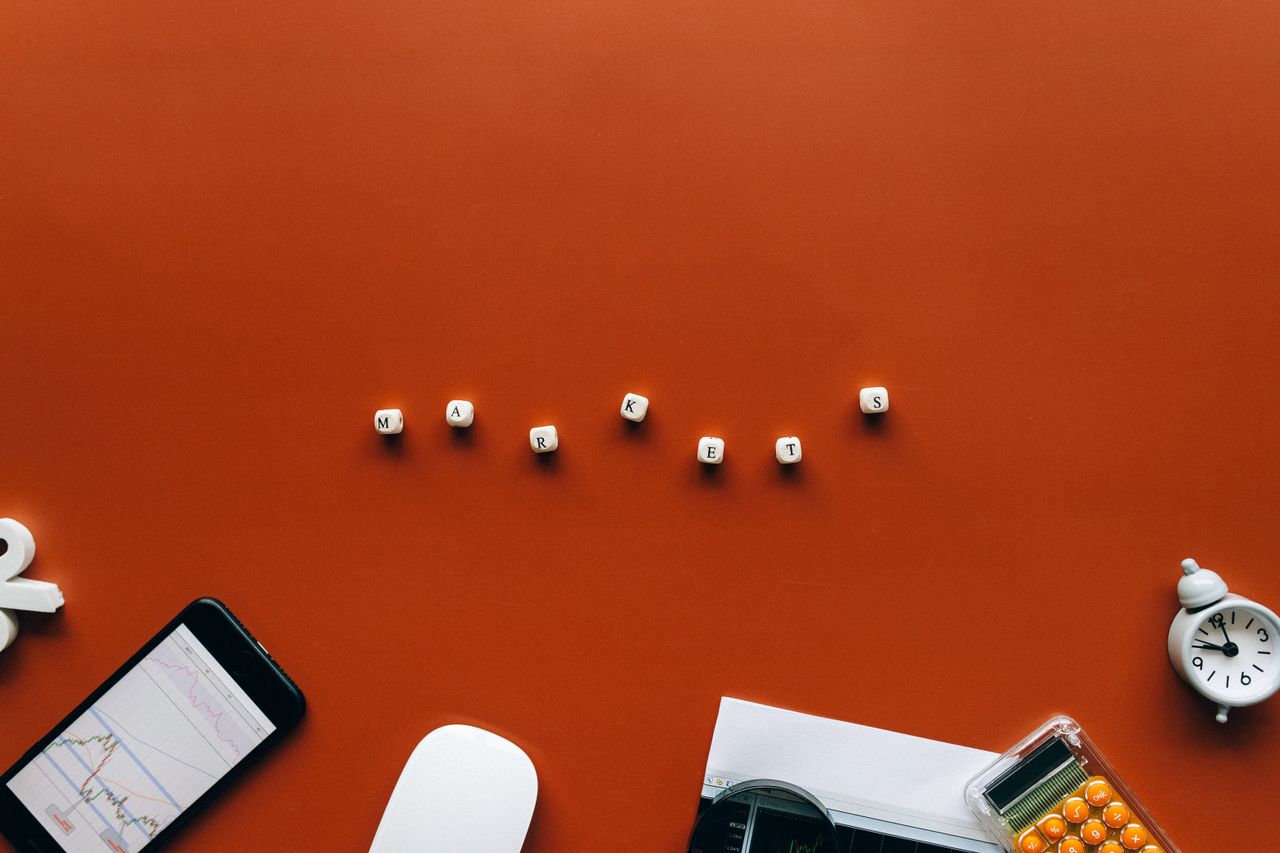 team-03 Creative still life with financial tools and the word MARKETS on an orange background.